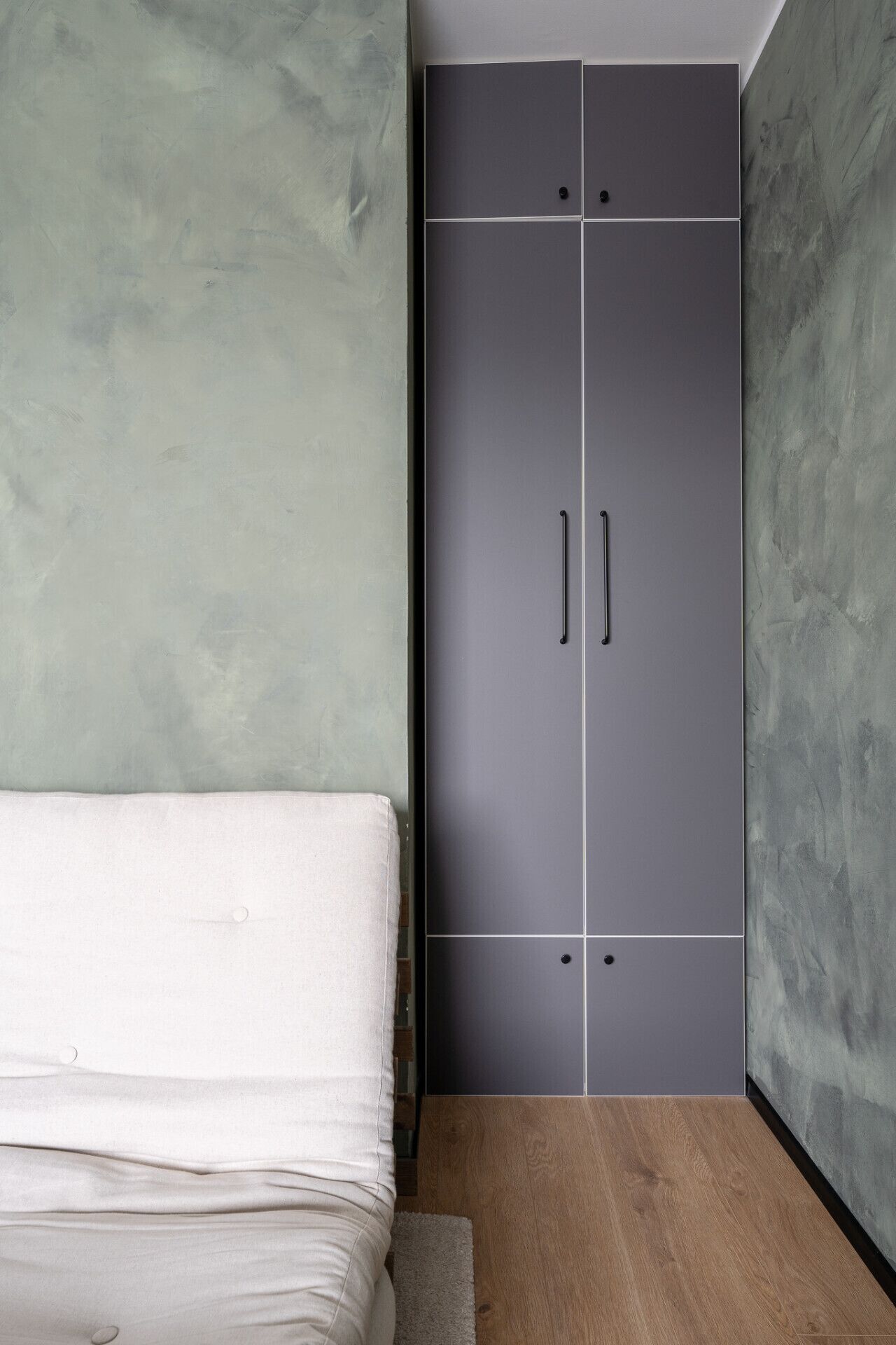 A bedroom with a bed, a grey wardrobe, and a wooden floor.