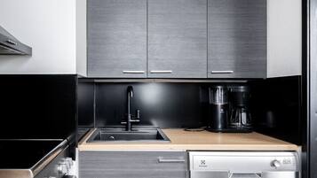 A modern kitchen with grey cabinetry, a stainless steel dishwasher, a coffee maker, and a wooden countertop.