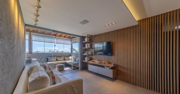 Een moderne woonkamer met een grote televisie, een bank en uitzicht op de oceaan.