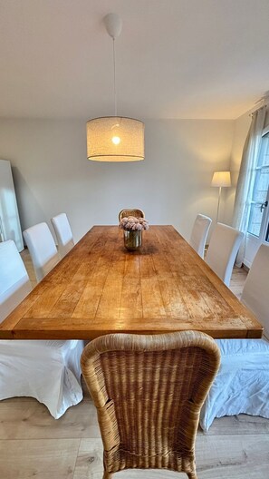 Ein Esszimmer mit Holztisch, weißen Stühlen, einem Korbstuhl und einer Pendelleuchte.