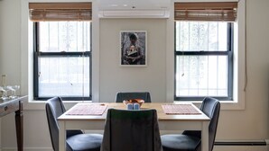 Uma sala de jantar com uma mesa de madeira, quatro cadeiras e duas janelas com persianas.
