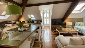 Una habitación estilo loft con cocina, comedor y sala de estar, que cuenta con vigas de madera a la vista, tragaluces y un televisor de pantalla plana.