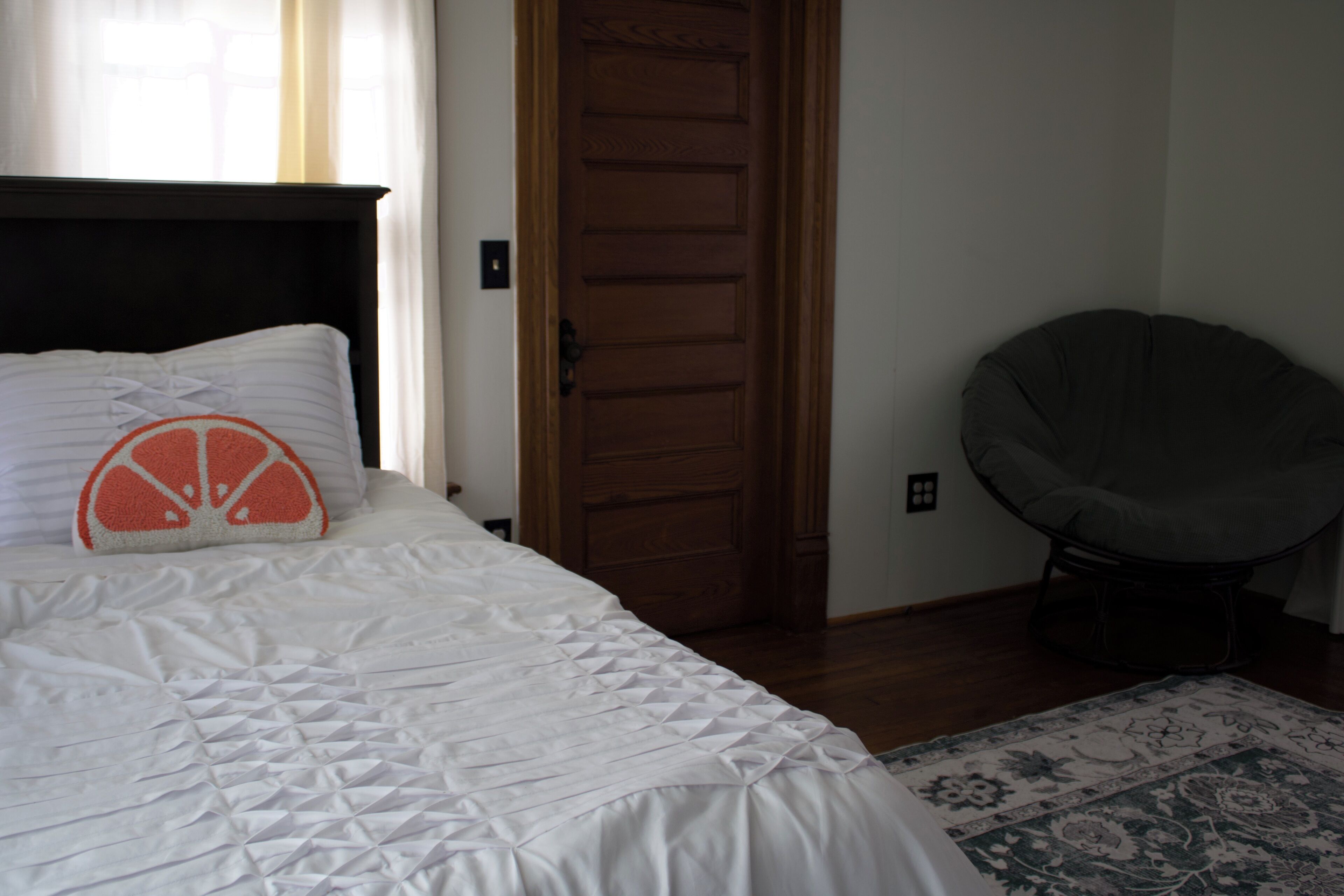 A bedroom with a bed, a wooden door, and a chair.