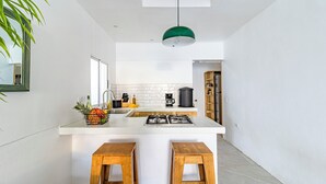 A modern kitchen with a white countertop, two wooden stools, a hanging green pendant light, and a tiled backsplash. - Cool house with Pool at only steps from the Beach and Surf (Carmen Beach)