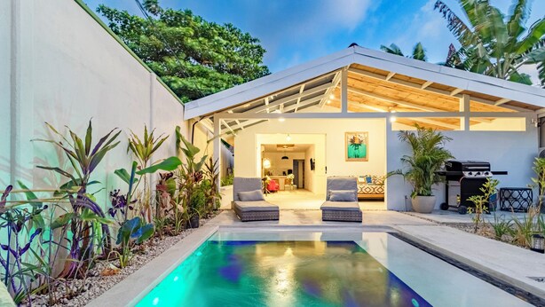 A modern outdoor pool area with a covered seating area, surrounded by lush plants. - Cool house with Pool at only steps from the Beach and Surf (Carmen Beach)