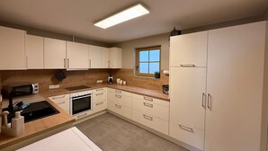 Una cocina moderna con armarios blancos, horno empotrado, microondas y ventana.