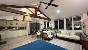 Un vaste espace de vie doté d’un haut plafond, de poutres apparentes, d’un ventilateur de plafond, d’un canapé, d’une table à manger avec des chaises, et d’un coin cuisine avec un comptoir et des appareils électroménagers.
