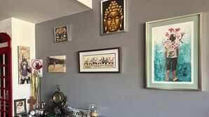 Une pièce dont un mur gris est décoré de divers tableaux encadrés, notamment une tête de Bouddha, une peinture représentant une femme tenant des fleurs et une photographie encadrée.