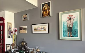 Ein Zimmer mit grauer Wand, verziert mit verschiedenen gerahmten Kunstwerken, darunter ein Buddha-Kopf, ein Gemälde einer Frau mit Blumen und ein gerahmtes Foto.