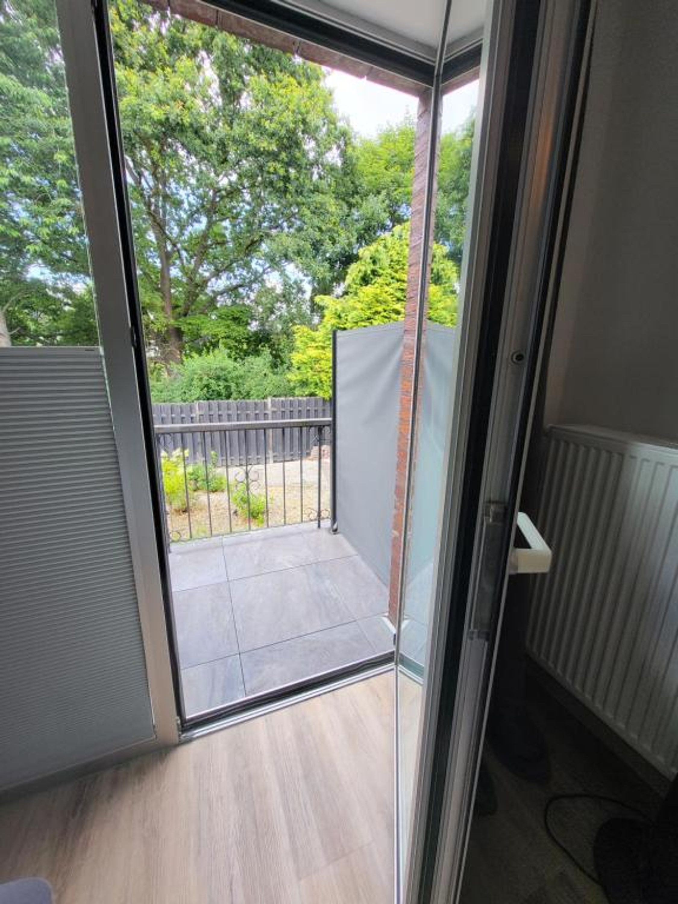 A room with a sliding glass door leading to a balcony with a view of trees and a fence.