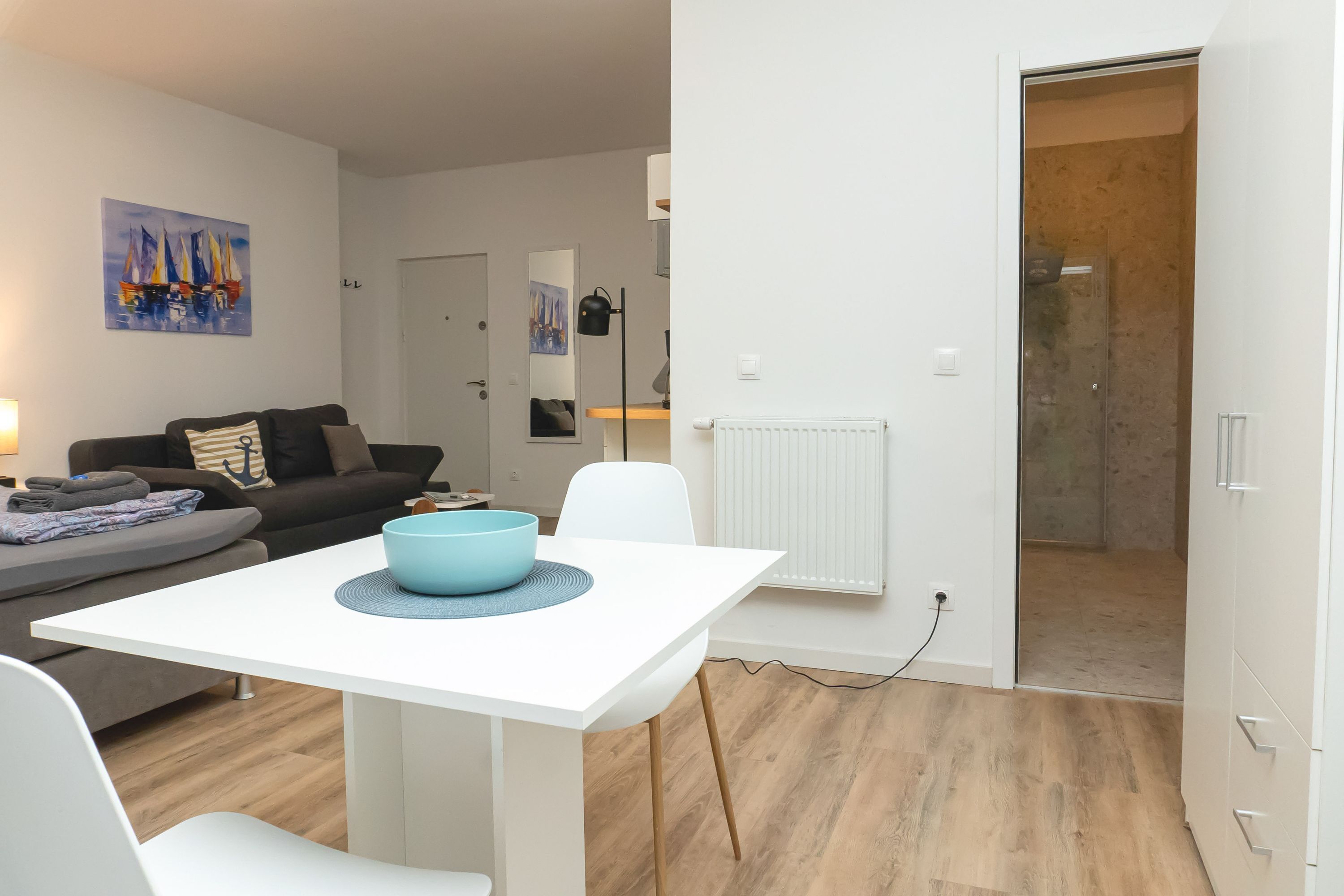 A modern living room with a white table, a blue bowl, a grey sofa, and a painting of sailboats.