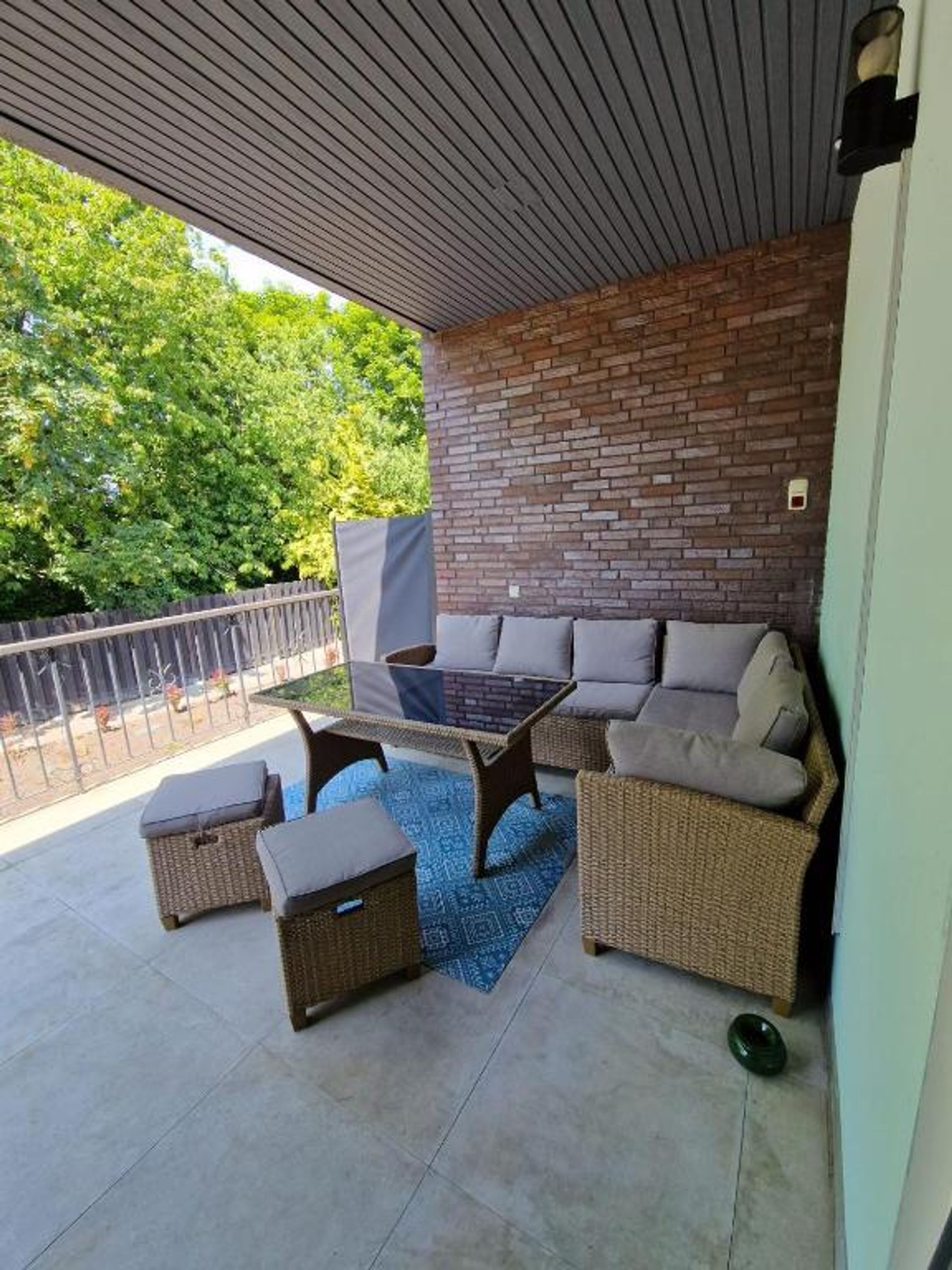 En overdækket terrasse med murstensvæg, fletmøbler og et blåt tæppe med mønster.