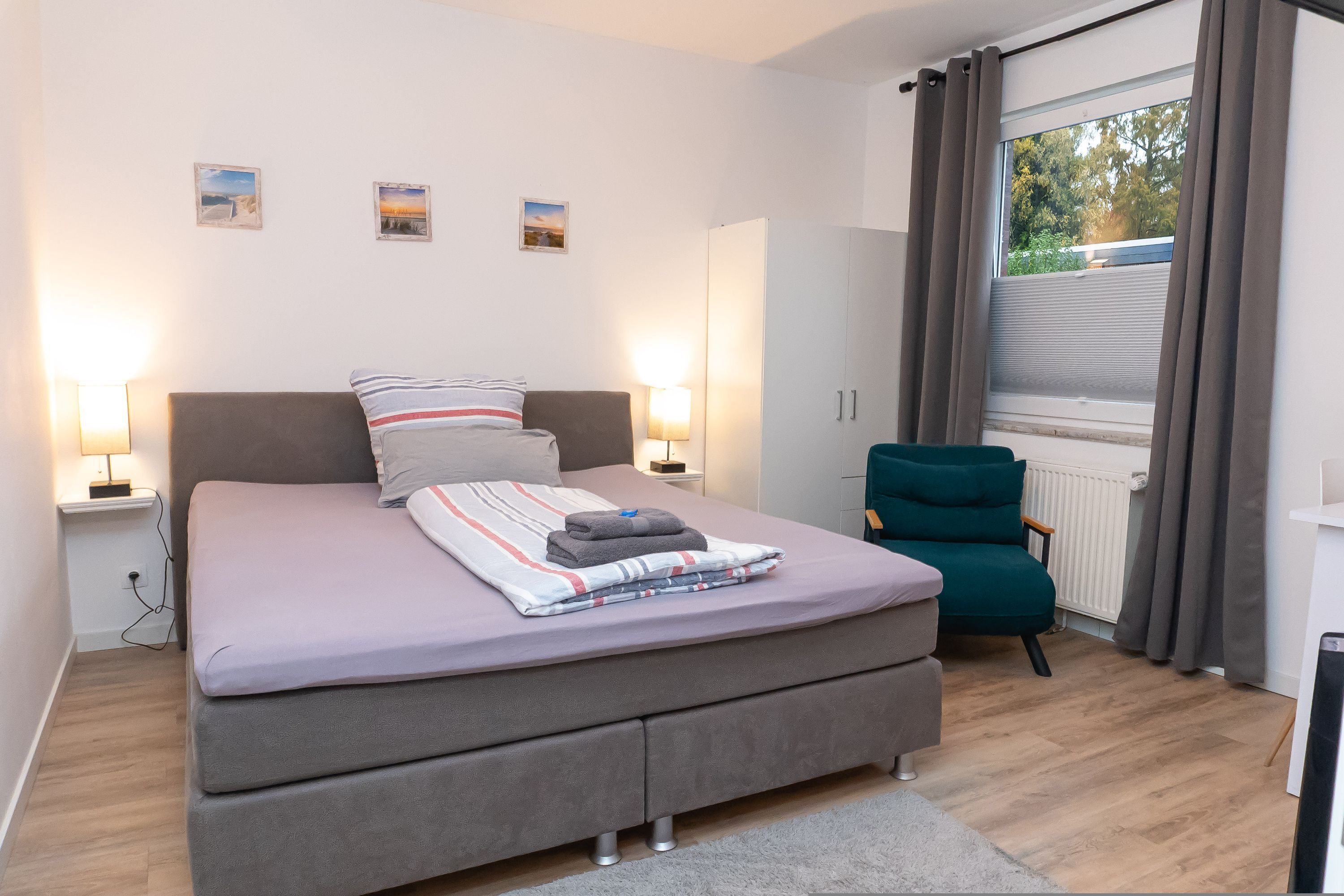 A bedroom with a bed, bedside lamps, a chair, and a window with curtains.