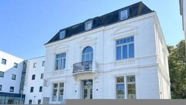 A white building with a classic architectural style, featuring a symmetrical facade, large windows, and a balcony with ornate railings. - Infinity Stay: Nordsee Apartments (Wilhelmshaven)