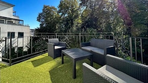 An outdoor patio with modern furniture, a metal fence, and lush greenery. - Infinity Stay: Nordsee Apartments (Wilhelmshaven)