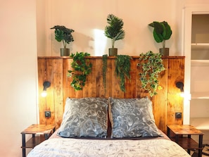 A bedroom with a wooden headboard, two bedside lamps, a bed with patterned bedding, and three potted plants on the headboard. - Le Bleuet - 5mn walk from the lake - Private parking lot (Aix-les-Bains)