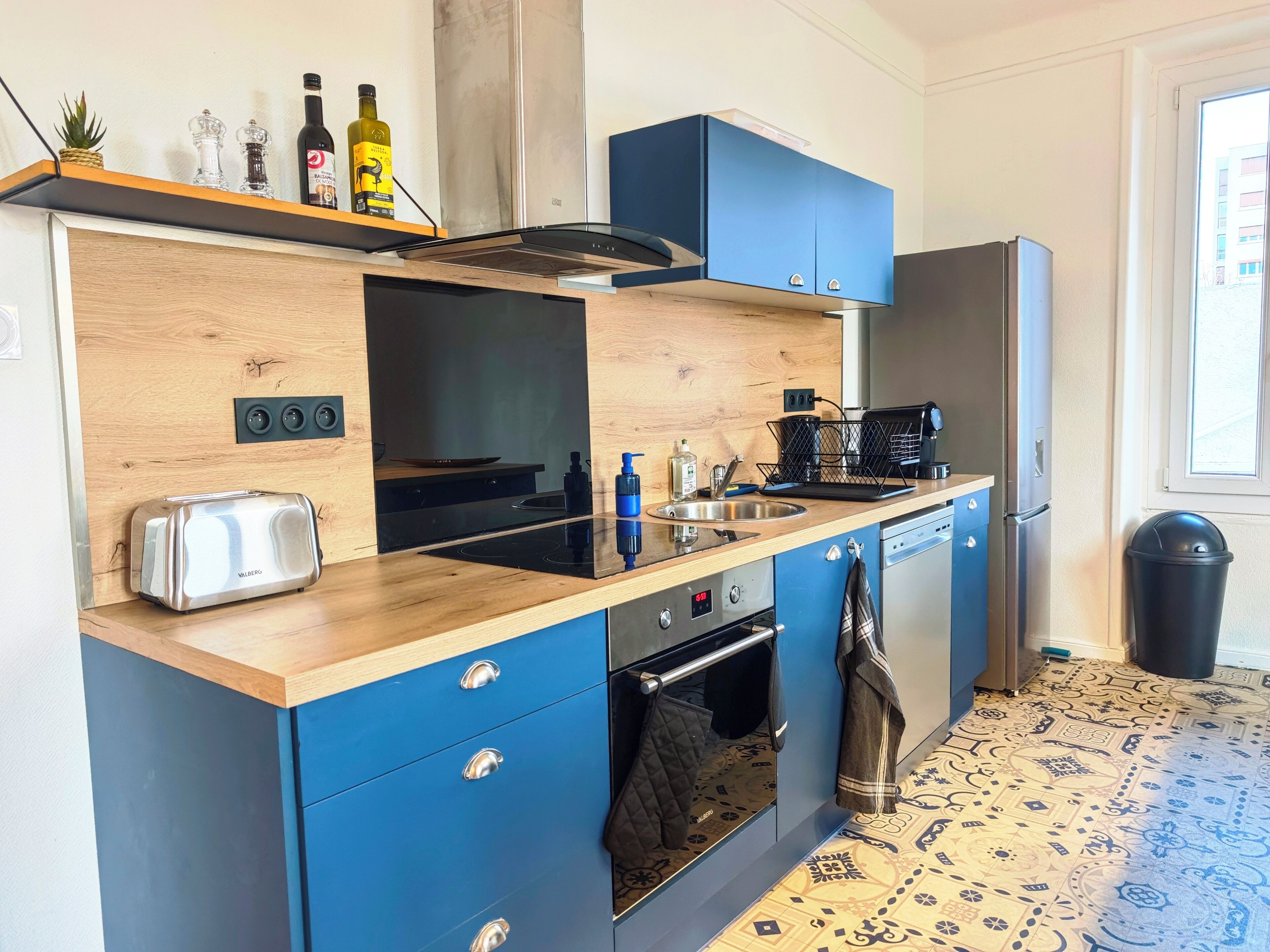 A compact kitchen with a wooden countertop, a built-in oven, a coffee machine, and a refrigerator.