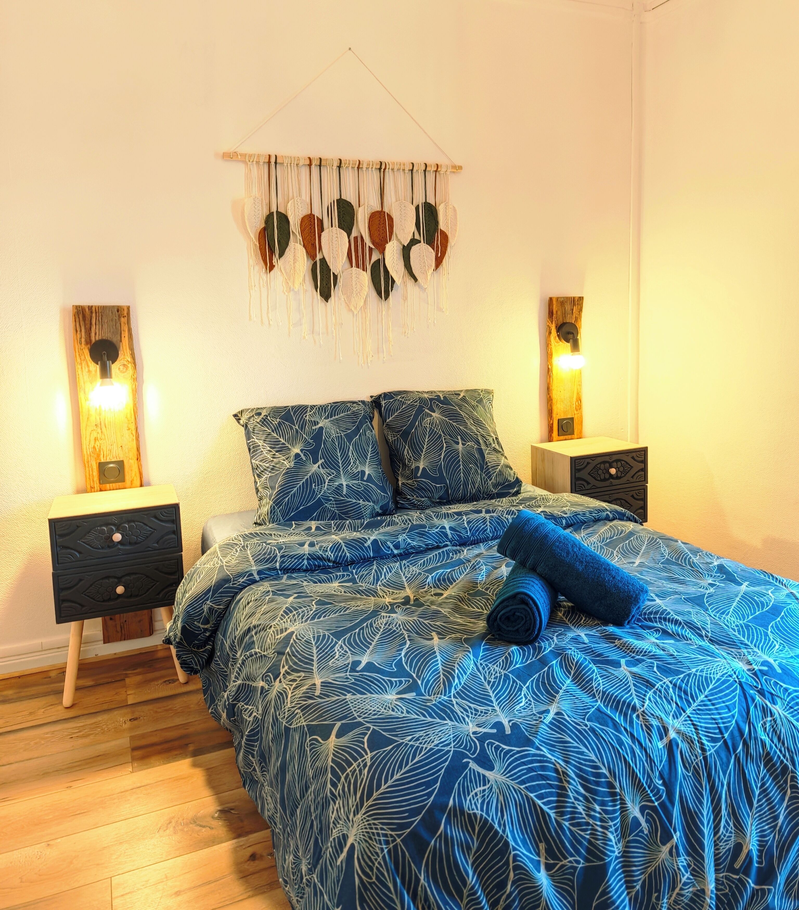 A bedroom with a bed, two nightstands, a wall hanging, and a wooden floor.