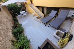 Eine Terrasse mit einem weißen Tisch, Stühlen, einem kleinen weißen Korb und einem gelben Gartenschlauch.