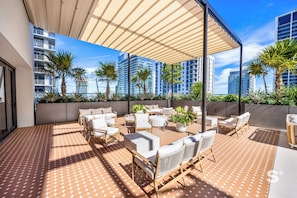 A rooftop patio with outdoor seating, palm trees, and a view of high-rise buildings. - High-Rise Condo in DTW Miami -Pool & Gym (Miami)