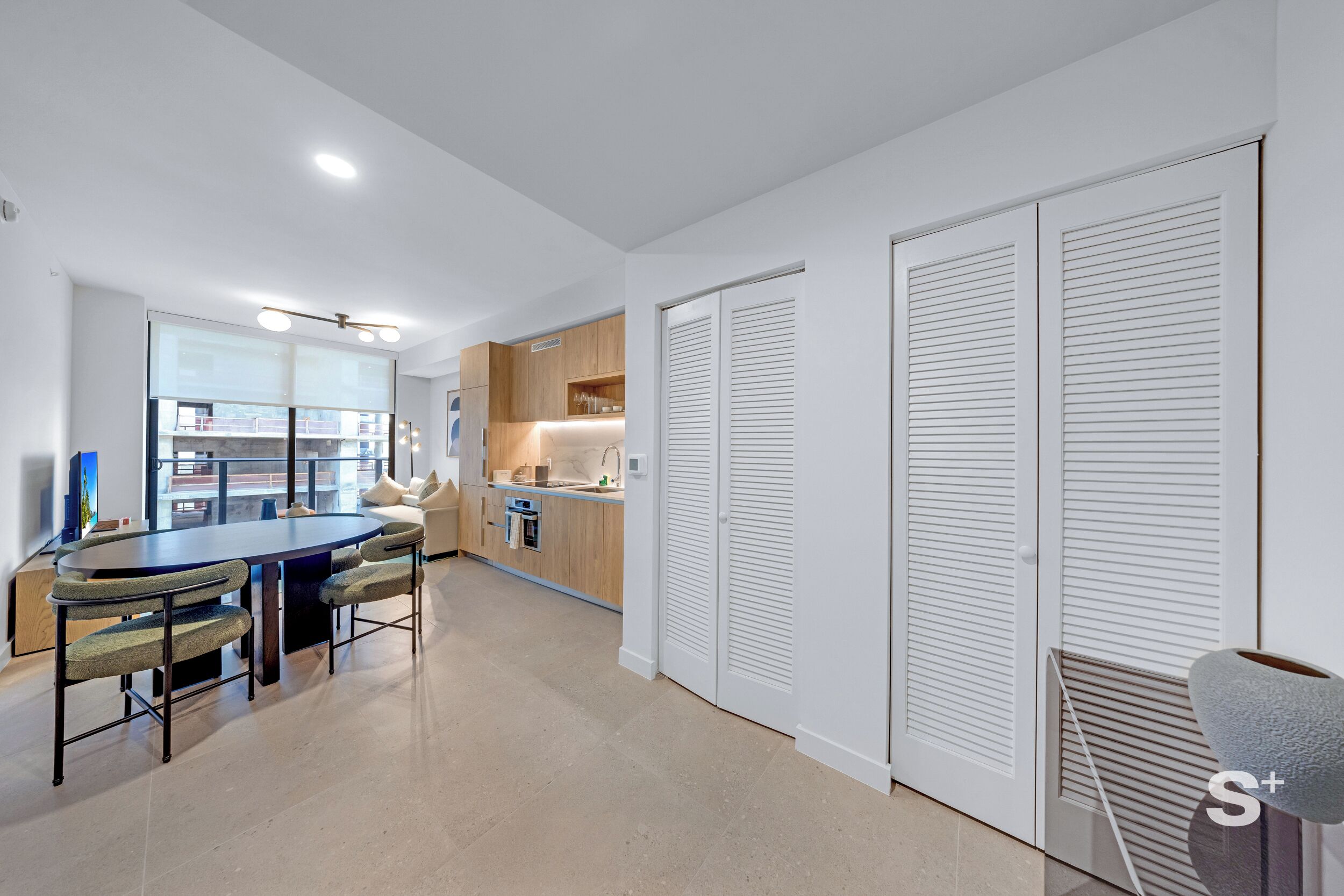 A modern kitchen with a dining area, white cabinetry, and a large window.