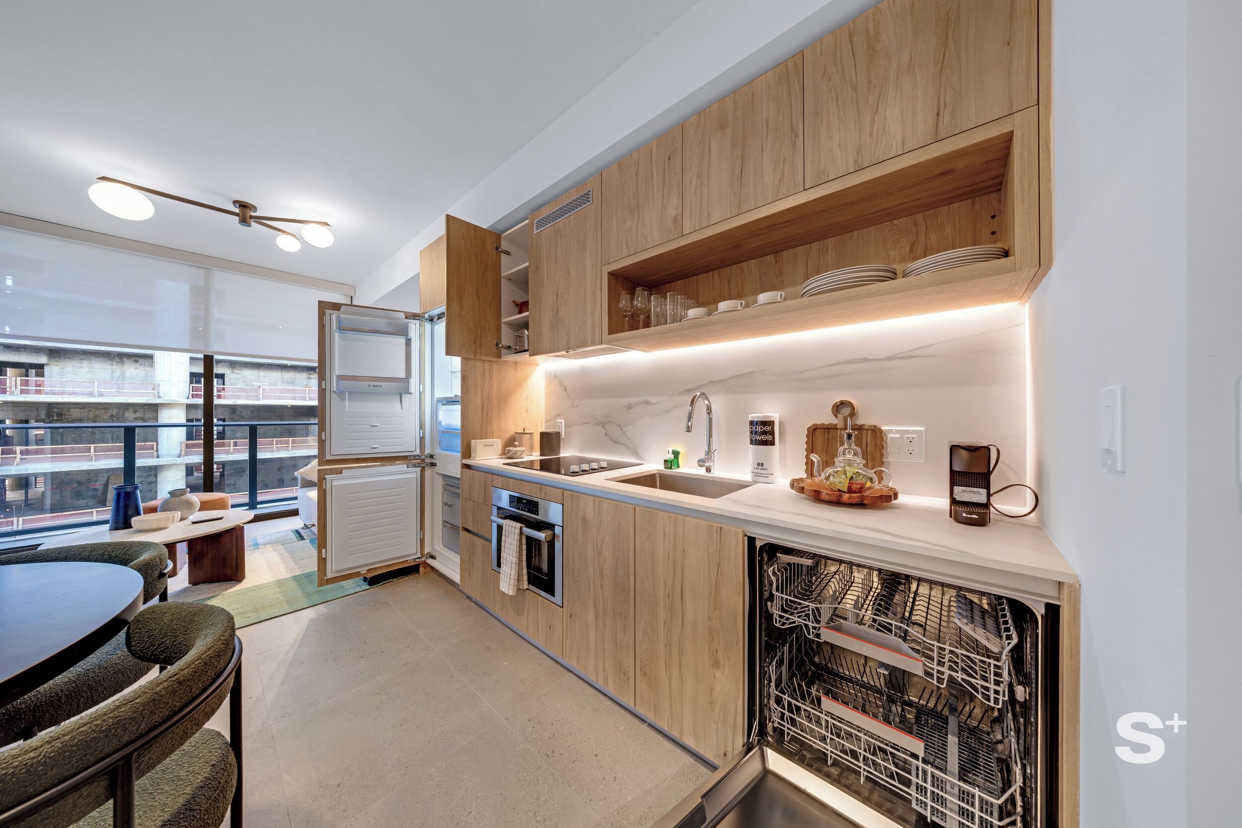 A modern kitchen with wooden cabinets, a built-in dishwasher, and a view of the city.