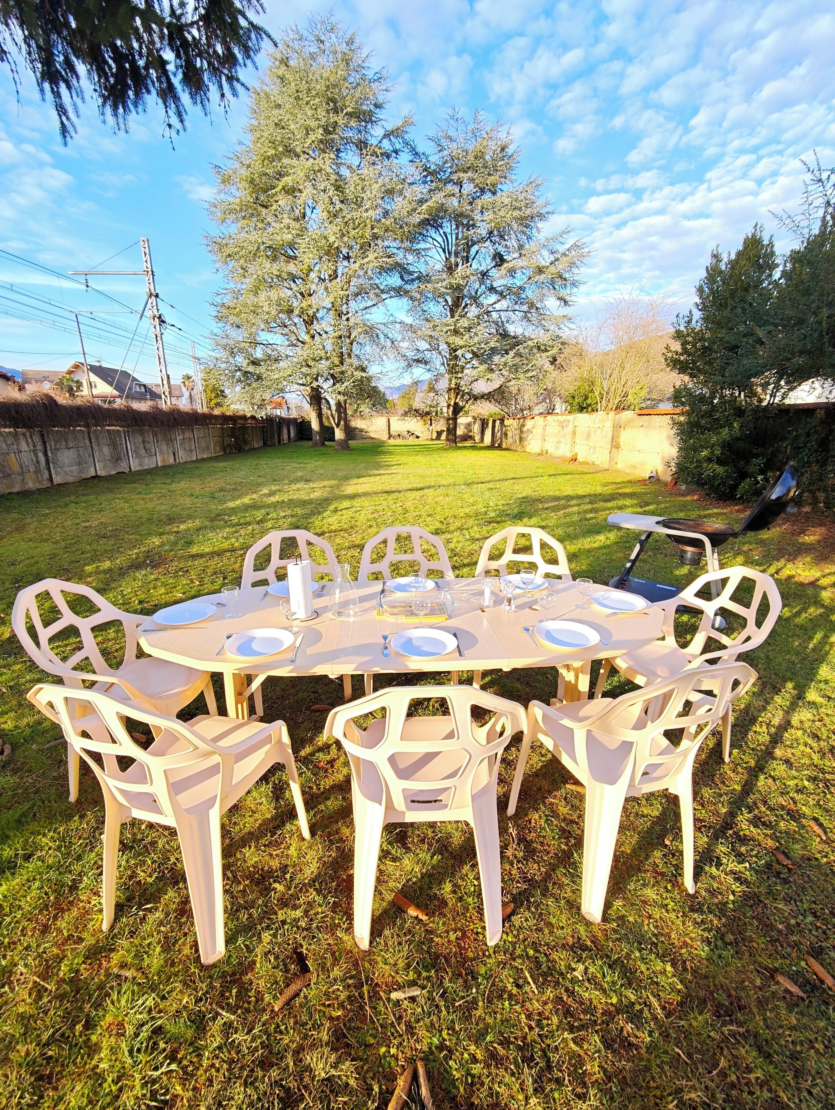 Un espace extérieur aménagé pour les repas, avec une table ronde et des chaises, entouré de pelouse et d’arbres.