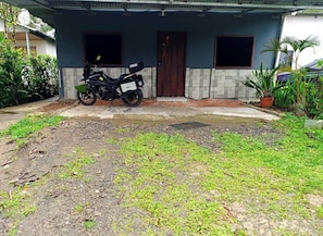 A residential building with a motorcycle parked in front, a tiled entrance, and a garden area with grass and plants.
