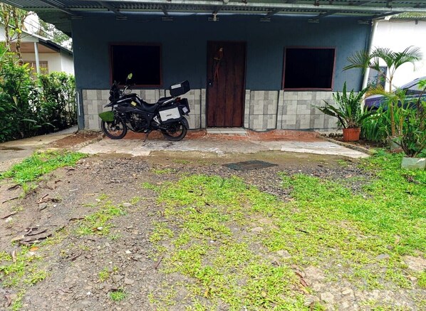 A residential building with a motorcycle parked in front, a tiled entrance, and a garden area with grass and plants.