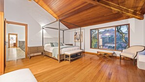A bedroom with a four-poster bed, wooden flooring, a large window with a mountain view, and a ceiling with exposed beams.