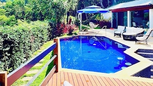 A wooden deck with a swimming pool, lounge chairs, and a covered seating area.