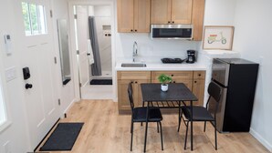 A modern kitchen with wooden cabinets, a stainless steel refrigerator, and a black dining table with two chairs. - Brand-New Furnished Studio ADU for Mid-Term Stays (San Mateo)