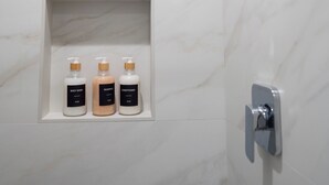 A bathroom with a shower, a marble wall, and a shelf with three bottles of toiletries. - Brand-New Furnished Studio ADU for Mid-Term Stays (San Mateo)