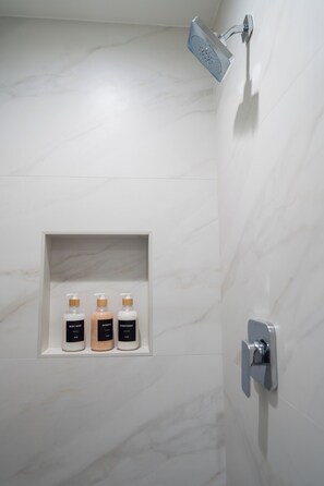 Ein Badezimmer mit Dusche, Marmorwand und Ablagefläche mit drei Toilettenartikeln.