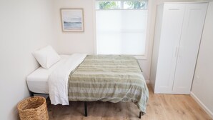 A bedroom with a bed, a window with blinds, a white wardrobe, and a wicker basket. - Brand-New Furnished Studio ADU for Mid-Term Stays (San Mateo)