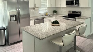 A modern kitchen with white cabinets, stainless steel appliances, a granite countertop, and pendant lighting.