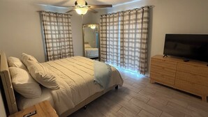 A bedroom with a bed, a TV, a ceiling fan, and curtains.