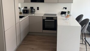 Eine moderne Küche mit weißen Schränken, einem eingebauten Backofen, einer Kaffeemaschine und einer kleinen Kochinsel mit Sitzgelegenheiten.