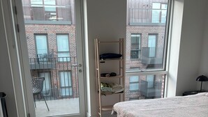 Ein Schlafzimmer mit einem Bett, einem Holzregal, einem Balkon mit Stuhl und Blick auf ein Backsteingebäude.