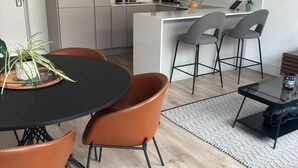 Eine moderne Küche mit weißen Schränken, einer zentralen Kochinsel mit Barhocker und einem Essbereich mit rundem Tisch und orangefarbenen Stühlen.