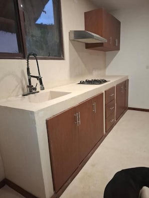 A compact kitchen with a sink, stove, and wooden cabinets. - Villas Ahal  (Tulum)
