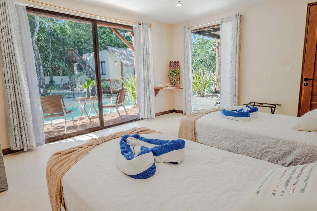 A hotel room with two beds, a large sliding glass door leading to a pool area, and a small table with a plant.