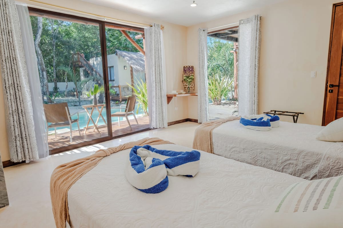 A hotel room with two beds, a large sliding glass door leading to a pool area, and a small table with a plant.