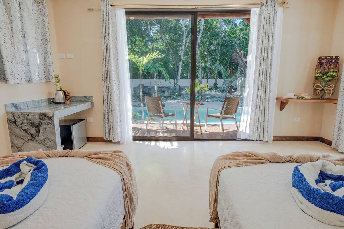 A hotel room with two beds, a marble desk, a small table, and a view of an outdoor pool area.