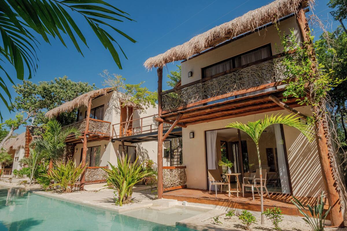 A resort with thatched-roof villas, a pool, and tropical landscaping.