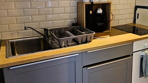 A kitchen with grey cabinets, a wooden countertop, a built-in brick backsplash, and a stainless steel sink. - The Queen's Hideaway (Fontainebleau)