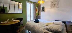 Ein Zimmer mit einem Bett, einem kleinen Tisch mit zwei Gläsern und Tellern, einem Stuhl und einem Fenster mit Vorhängen.