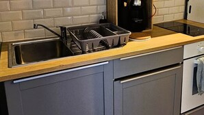 A modern kitchen with grey cabinets, a wooden countertop, a built-in brick backsplash, and a stainless steel sink. - The Queen's Hideaway (Fontainebleau)