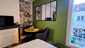 A compact room with a bed, a small round table with a chair, a television, and a window with a view of buildings. - The Queen's Hideaway (Fontainebleau)