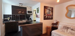 A compact kitchen with a black countertop, a microwave, and a sink. There's a framed picture on the wall and a decorative deer head on a side table. - La cachette de l'Alpiniste (Fontainebleau)